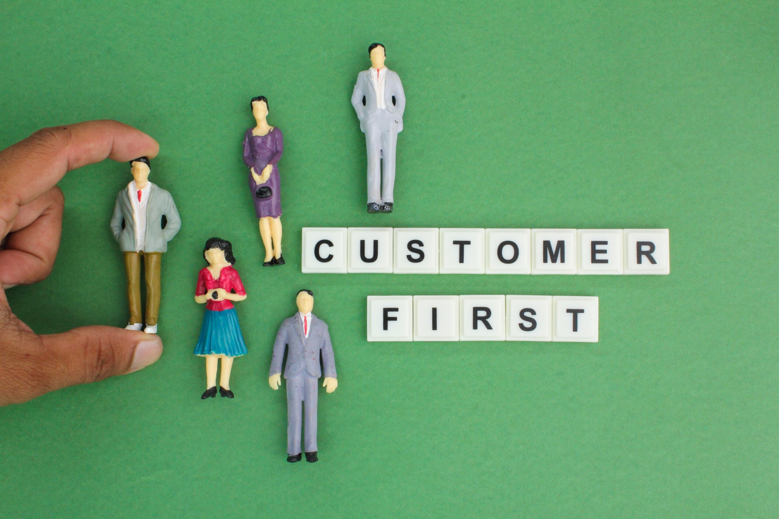 Small figurines surround the words “Customer First” on a green background.